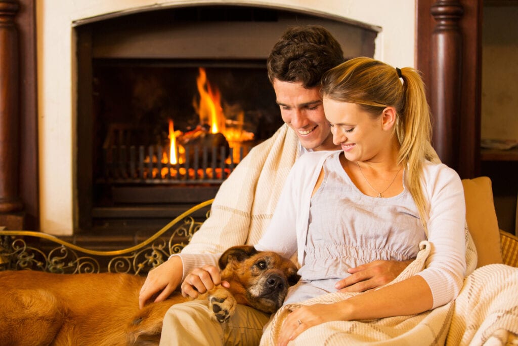 young couple sitting by fireplace with their pet dog